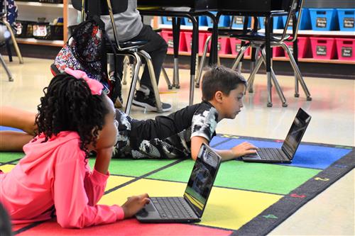 two students on floor looking at their chromebooks